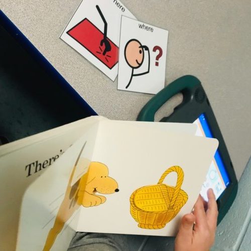 Photo with ‘Where’s Spot’ book upon and core symbols “where” and “here” on table with student’s AAC device in the background