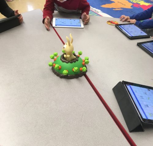Photo of a green toy on a table surrounded by tablets